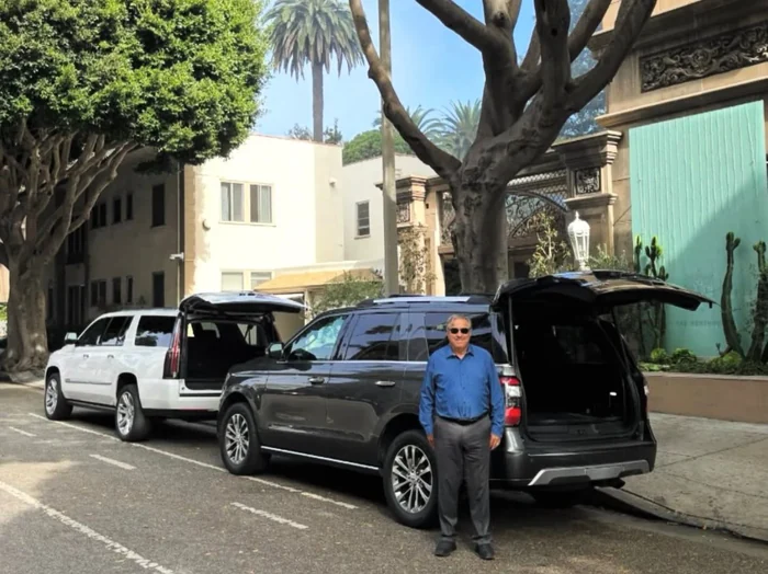 Chauffeur standing between two luxury SUVs on a Beverly Hills street